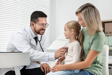 Doctor examining little girl with stethoscope and her mother in hospital