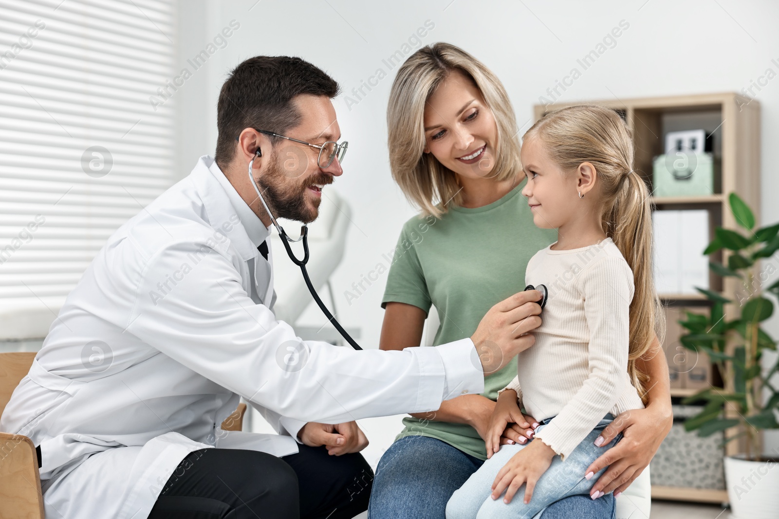 Photo of Doctor examining little girl with stethoscope and her mother in hospital