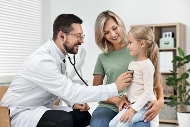 Doctor examining little girl with stethoscope and her mother in hospital