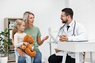 Photo of Doctor consulting little girl with teddy bear and her mother in hospital