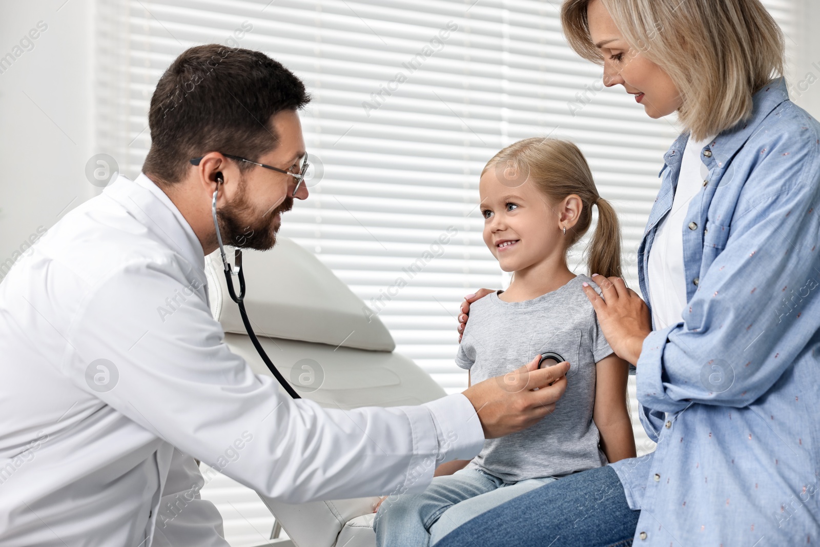 Photo of Doctor examining little girl with stethoscope and her mother in hospital