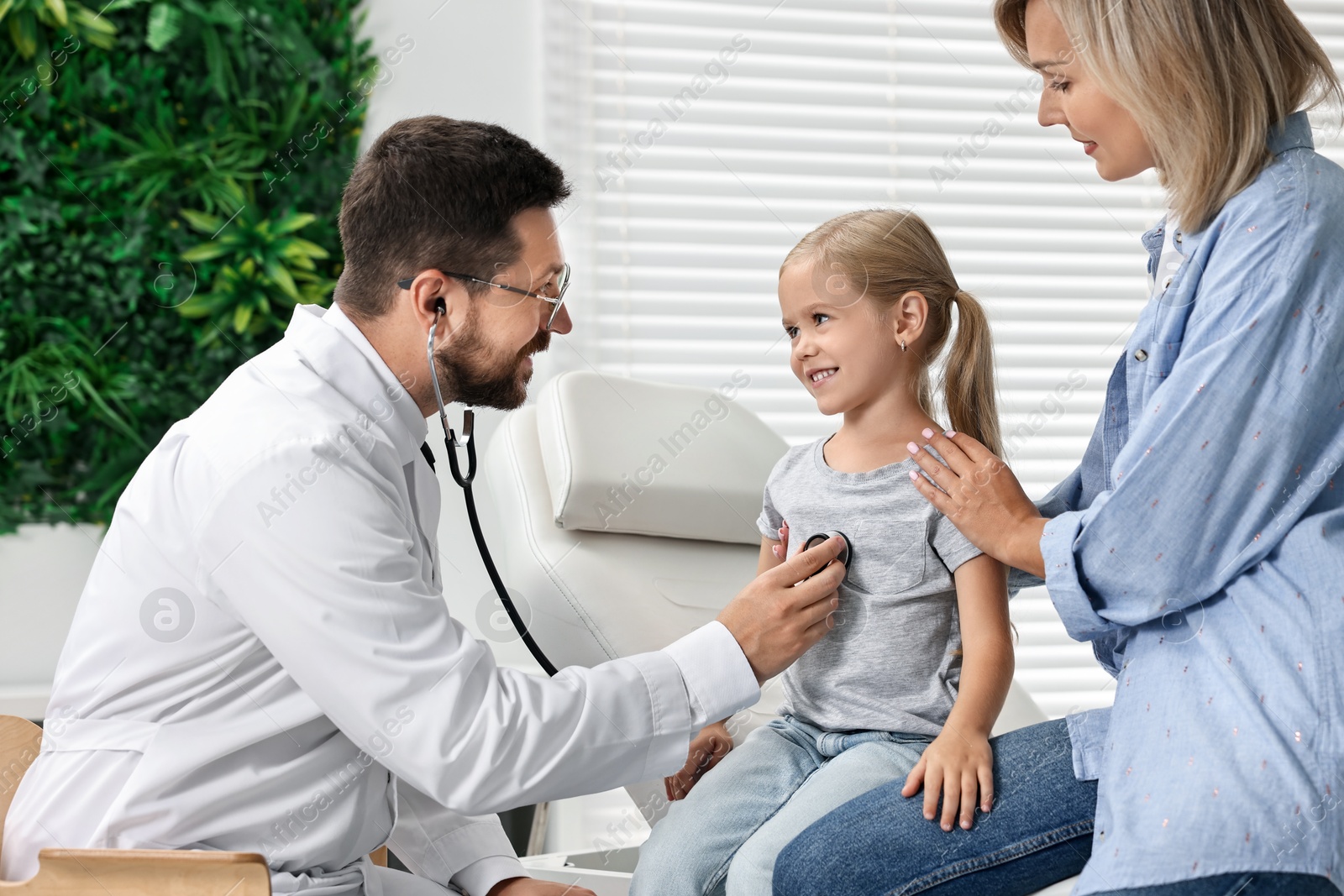 Photo of Doctor examining little girl with stethoscope and her mother in hospital