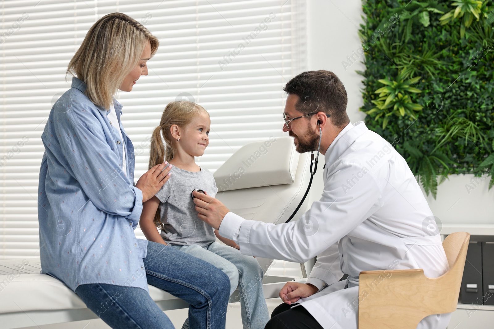 Photo of Doctor examining little girl with stethoscope and her mother in hospital