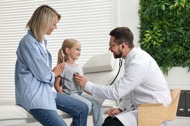 Photo of Doctor examining little girl with stethoscope and her mother in hospital