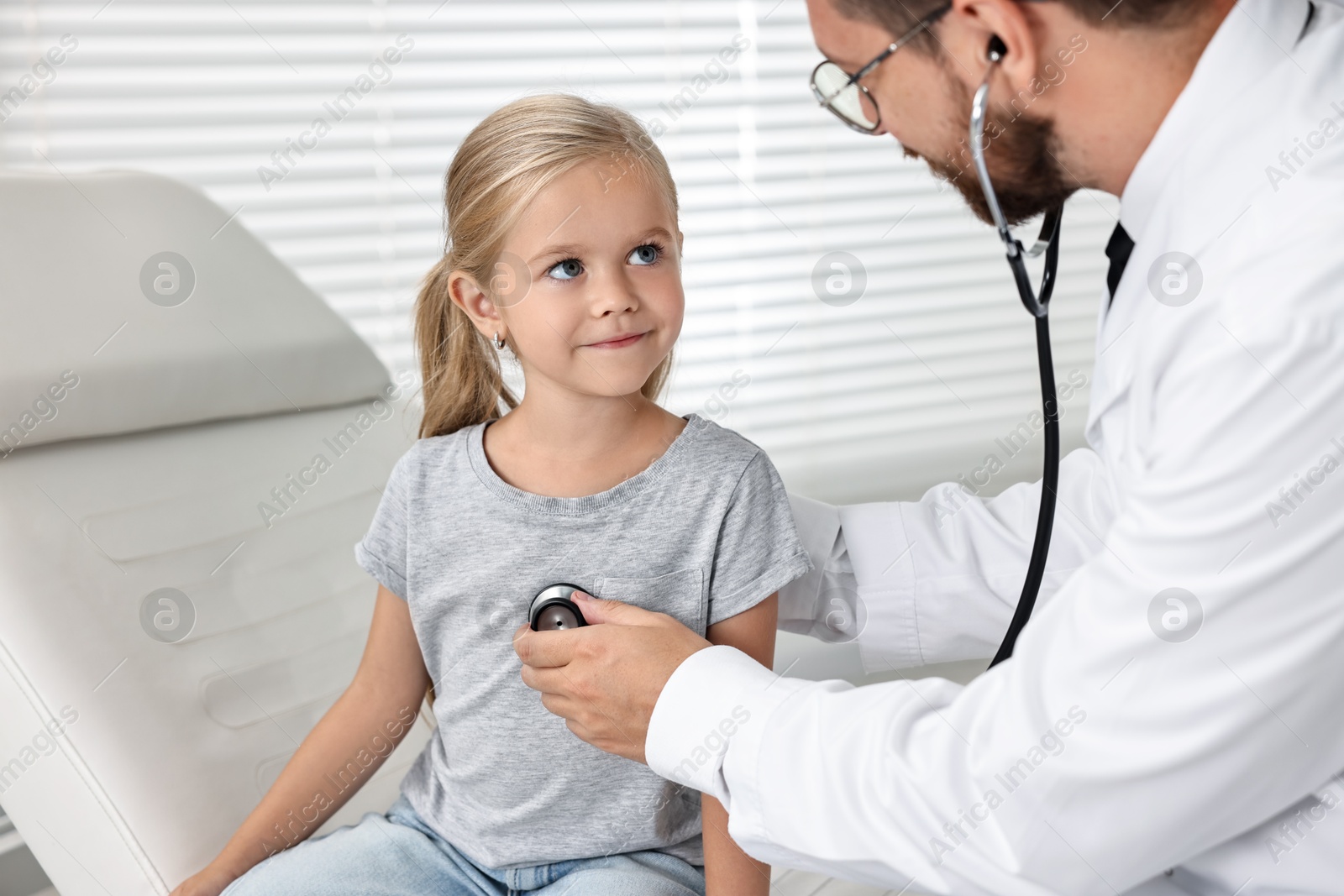 Photo of Doctor examining little girl with stethoscope in hospital, closeup