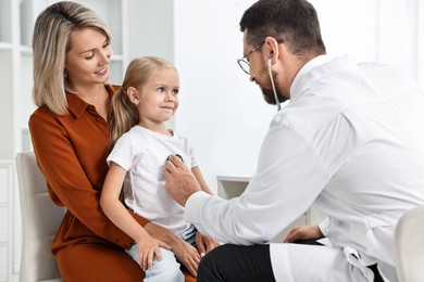 Photo of Doctor examining little girl with stethoscope and her mother in hospital