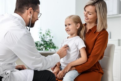 Photo of Doctor examining little girl with stethoscope and her mother in hospital