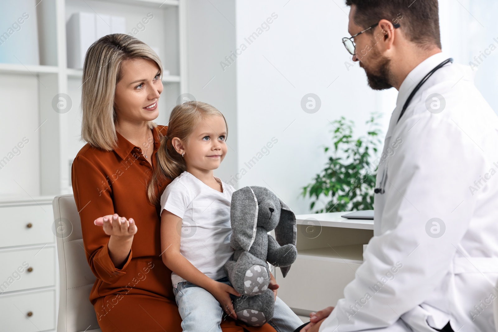 Photo of Doctor consulting little girl with toy and her mother in hospital