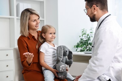 Doctor consulting little girl with toy and her mother in hospital