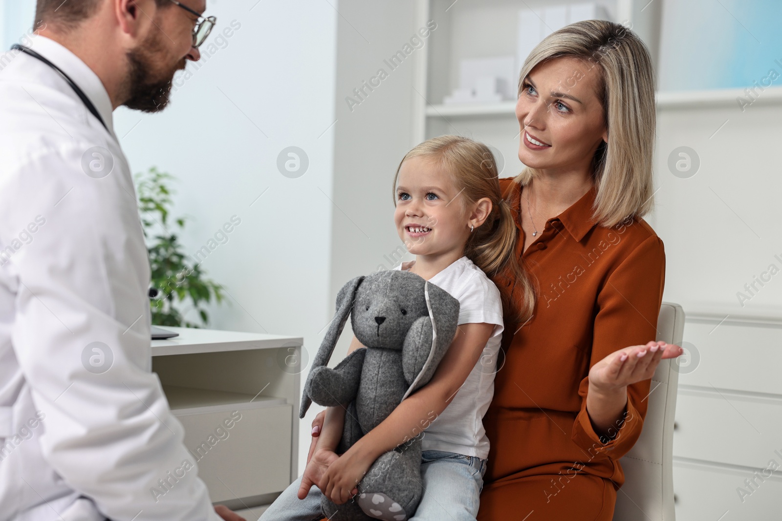 Photo of Doctor consulting little girl with toy and her mother in hospital