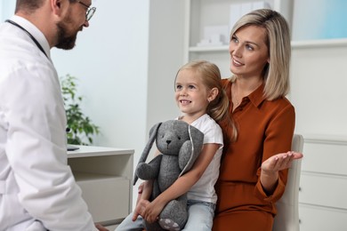 Doctor consulting little girl with toy and her mother in hospital