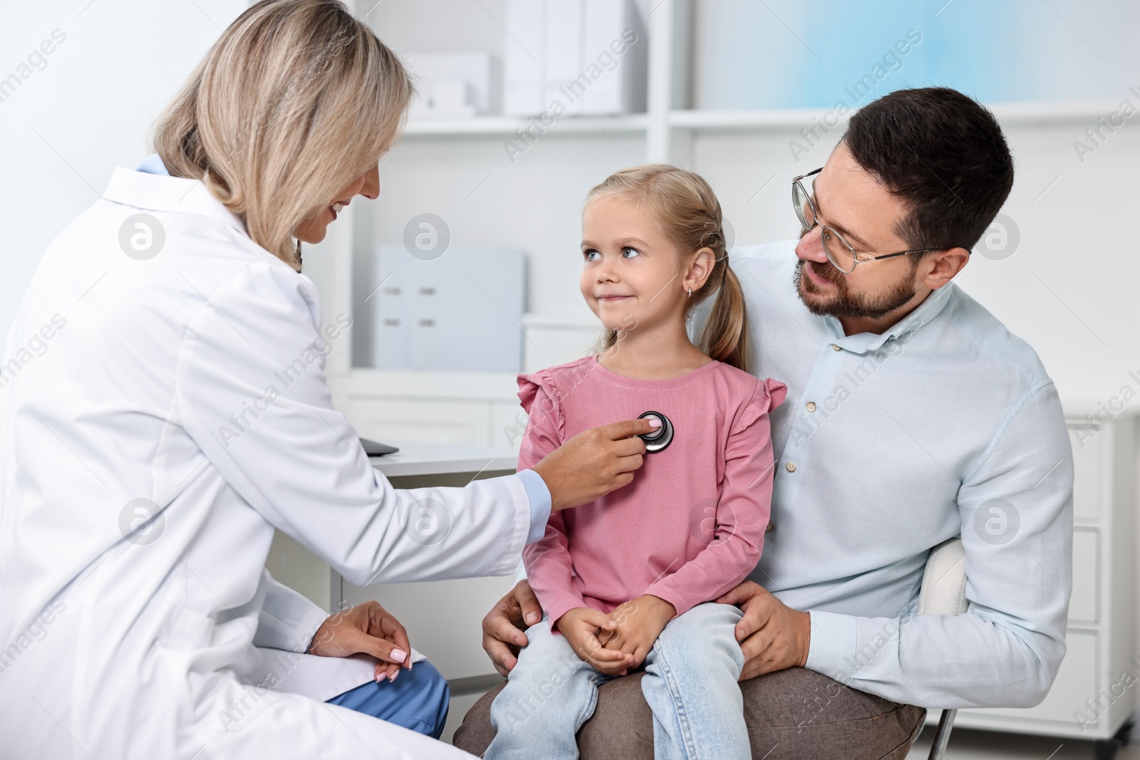 Photo of Doctor examining little girl with stethoscope and her father in hospital