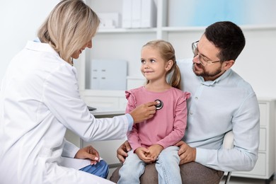 Doctor examining little girl with stethoscope and her father in hospital