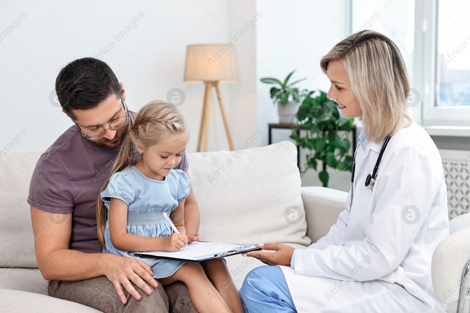 Photo of Doctor with clipboard consulting little girl and her father indoors