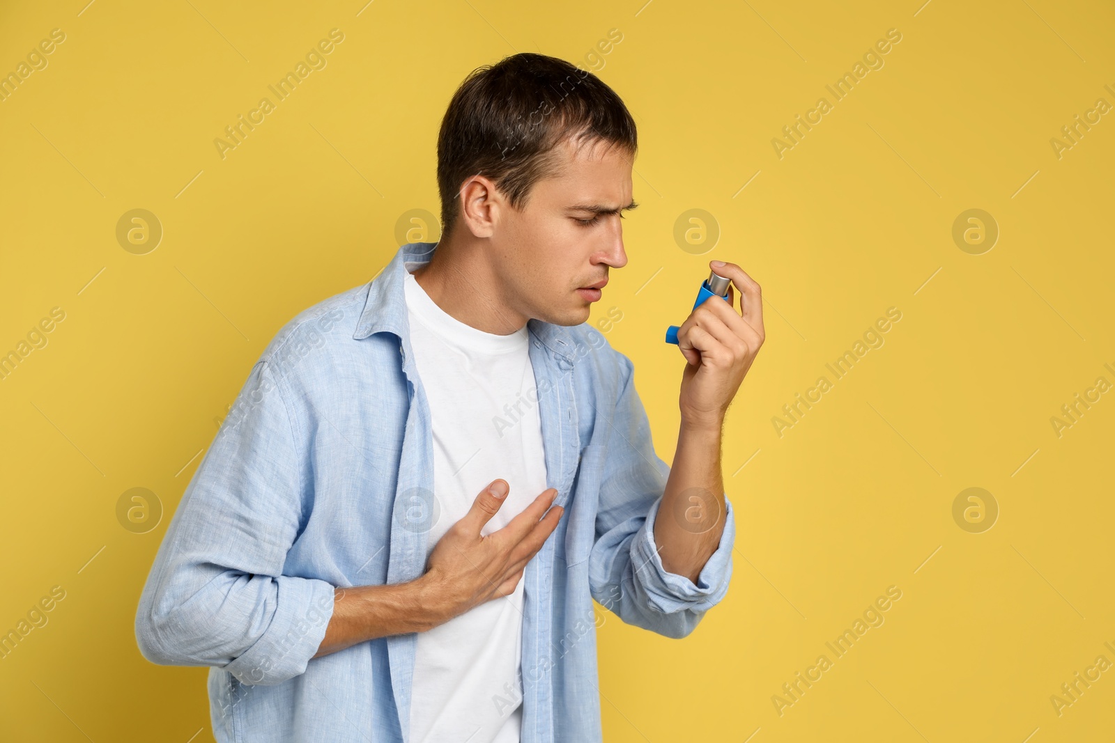 Photo of Man using asthma inhaler on yellow background