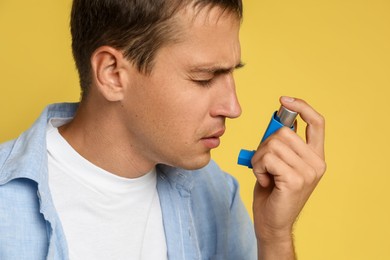 Man using asthma inhaler on yellow background