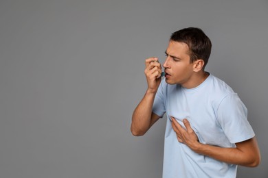 Man using asthma inhaler on grey background, space for text