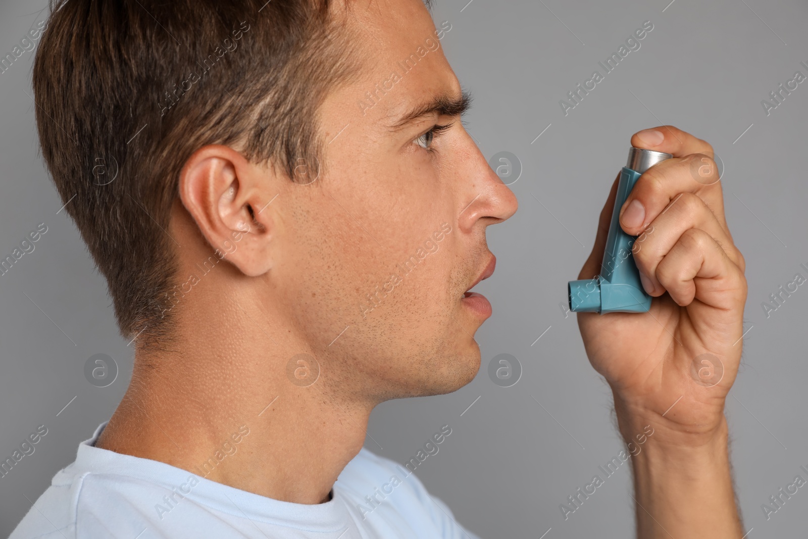 Photo of Man using asthma inhaler on grey background, closeup