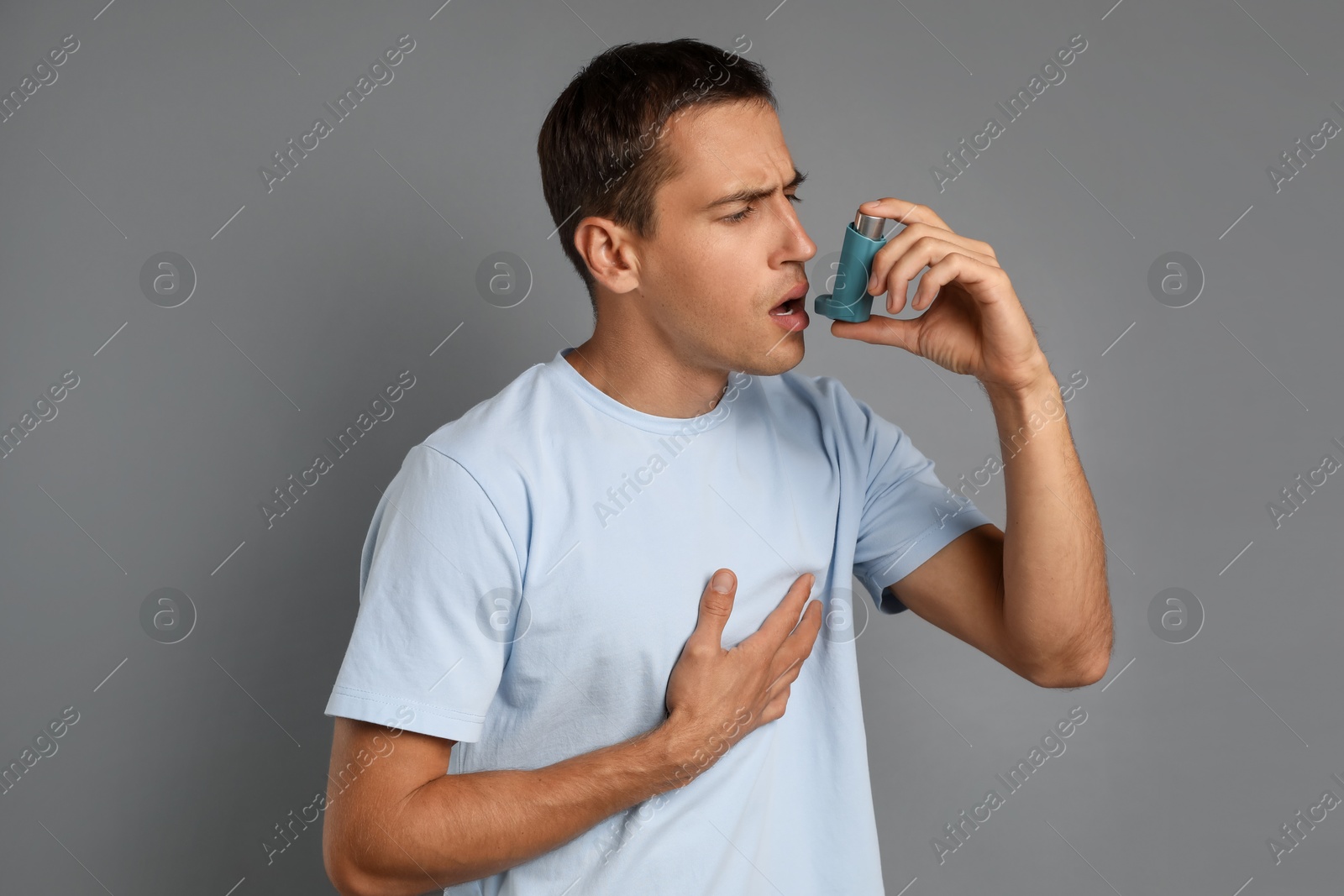 Photo of Man using asthma inhaler on grey background