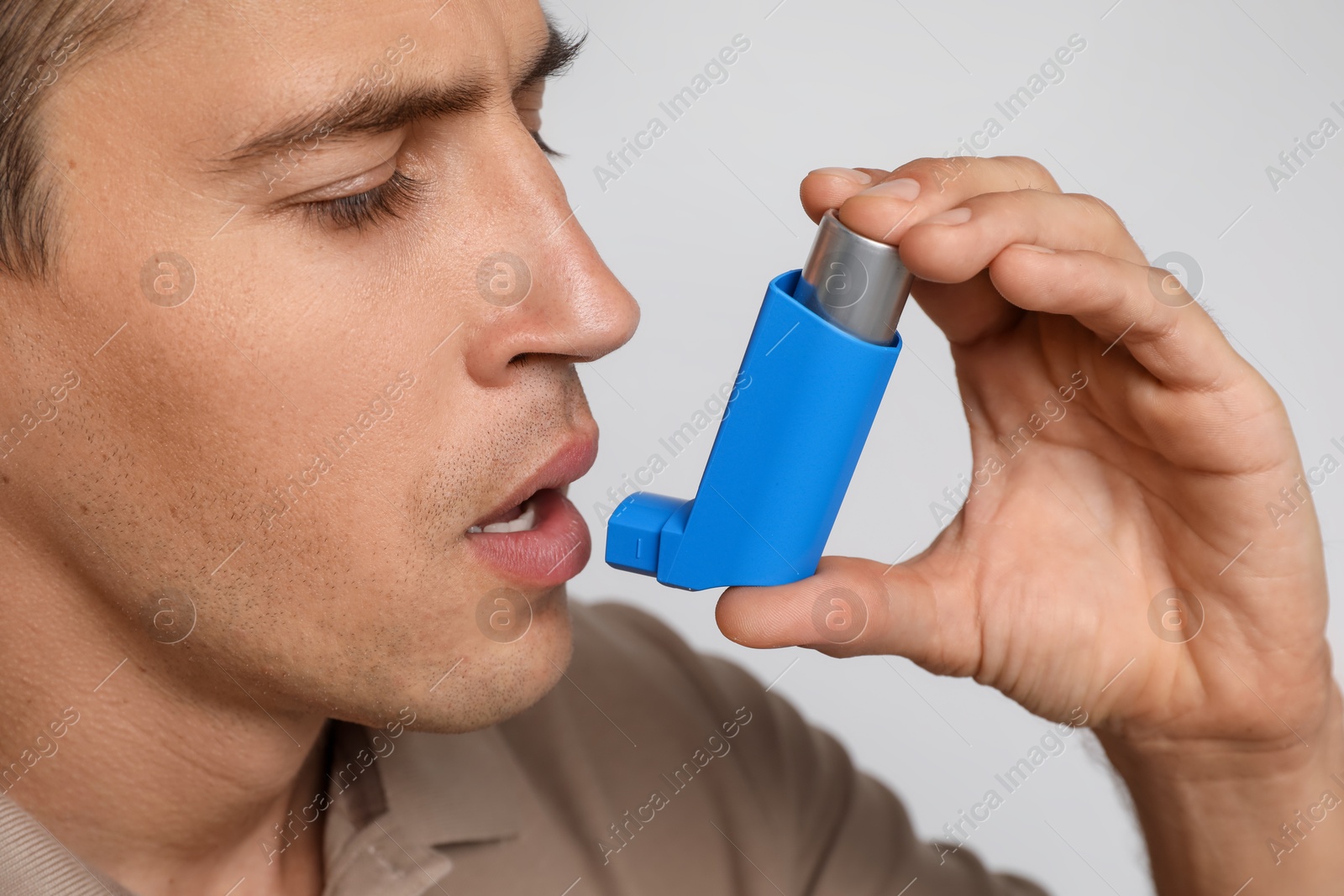 Photo of Man using asthma inhaler on light background, closeup