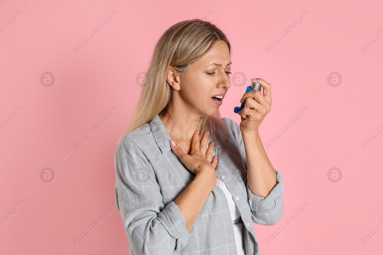 Photo of Woman using asthma inhaler on pink background