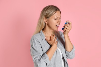 Woman using asthma inhaler on pink background