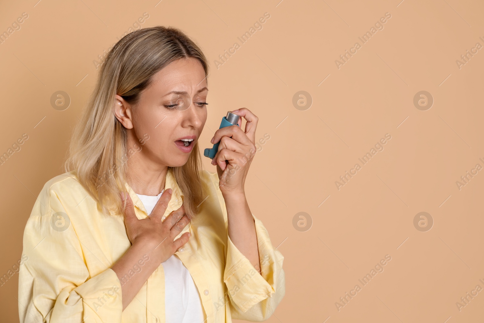 Photo of Woman using asthma inhaler on beige background, space for text