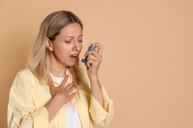 Photo of Woman using asthma inhaler on beige background, space for text