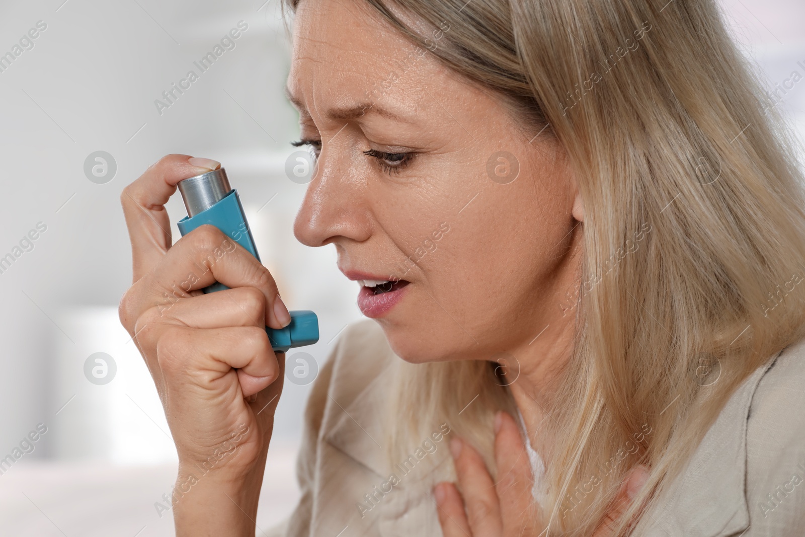 Photo of Woman using asthma inhaler at home, closeup