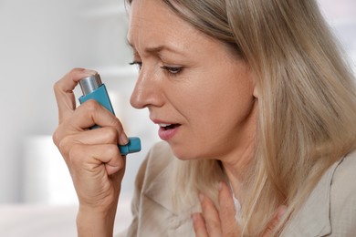 Woman using asthma inhaler at home, closeup