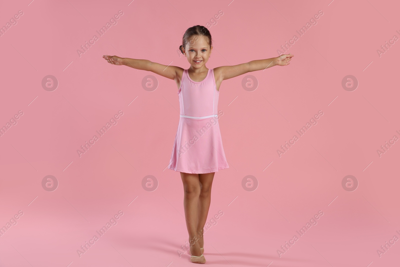 Photo of Little ballerina practicing dance moves on pink background