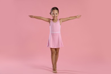 Photo of Little ballerina practicing dance moves on pink background