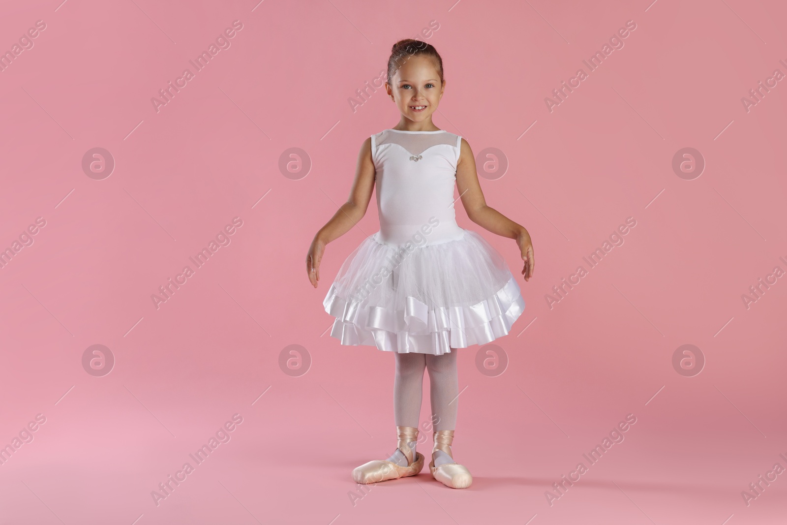 Photo of Little ballerina practicing dance moves on pink background