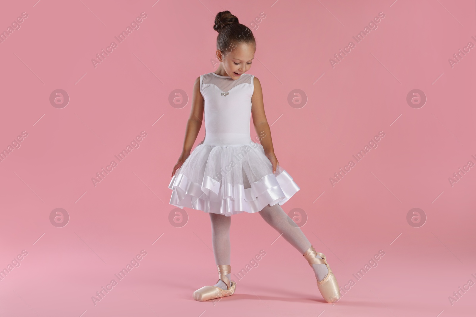 Photo of Little ballerina practicing dance moves on pink background