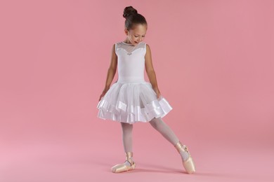 Photo of Little ballerina practicing dance moves on pink background