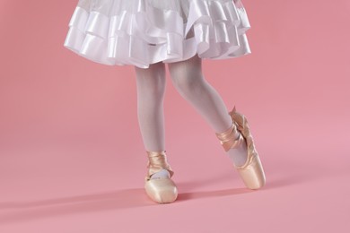 Photo of Little ballerina practicing dance moves on pink background, closeup