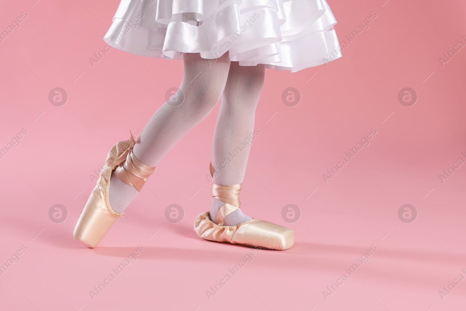 Photo of Little ballerina practicing dance moves on pink background, closeup