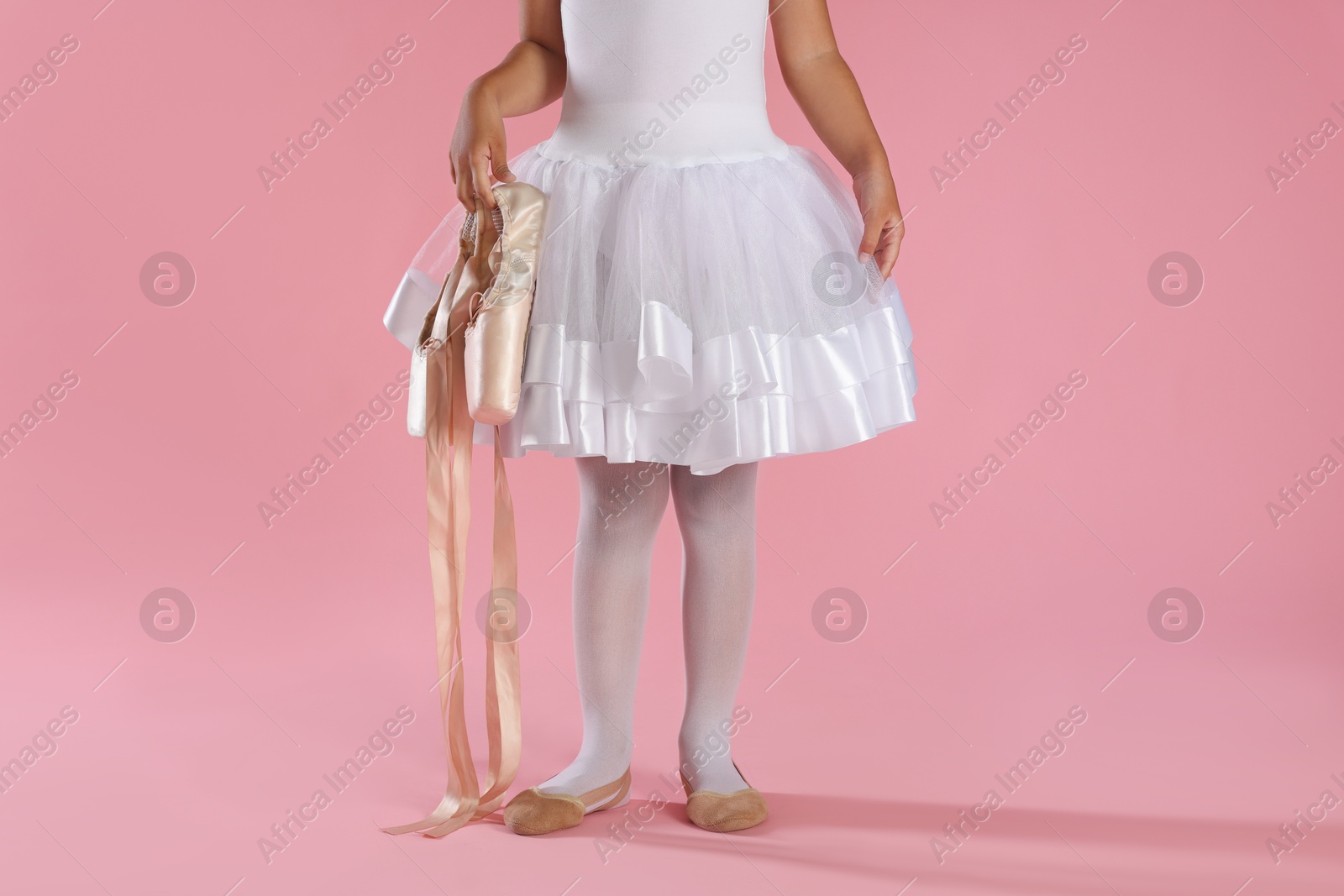 Photo of Little ballerina with pointe shoes on pink background, closeup