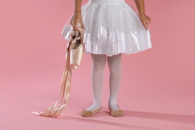 Photo of Little ballerina with pointe shoes on pink background, closeup