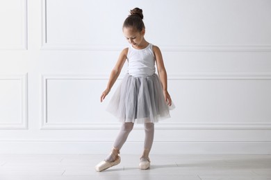 Photo of Little ballerina practicing dance moves near white wall indoors