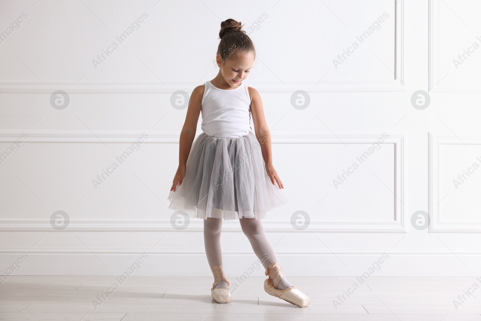 Photo of Little ballerina practicing dance moves near white wall indoors