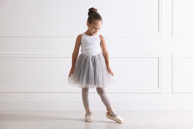 Photo of Little ballerina practicing dance moves near white wall indoors