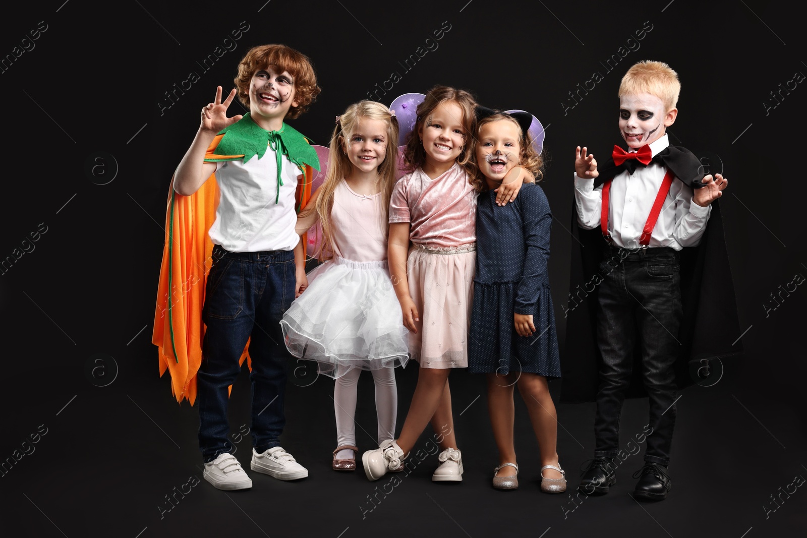 Photo of Funny children wearing costumes for Halloween celebration on black background