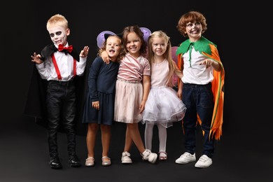 Photo of Funny children wearing costumes for Halloween celebration on black background