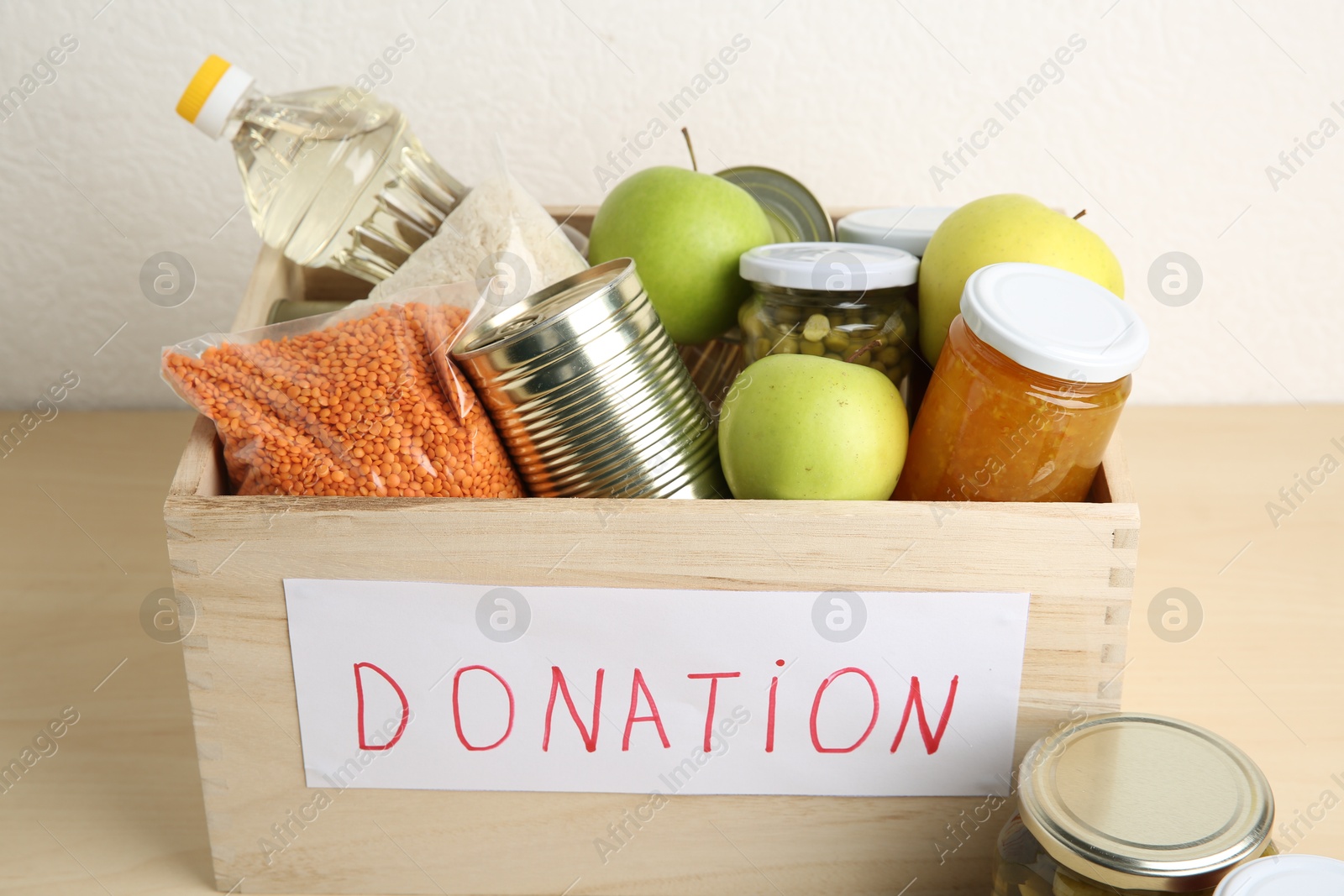 Photo of Different donation food products in crate on wooden table, closeup