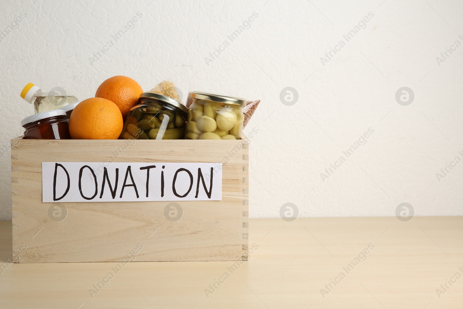 Photo of Different donation food products in crate on wooden table. Space for text