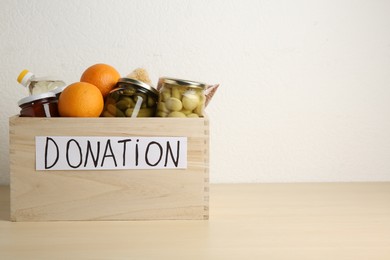 Photo of Different donation food products in crate on wooden table. Space for text