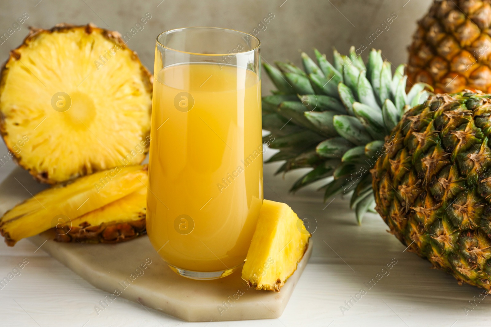 Photo of Tasty pineapple juice in glass and fresh fruits on white wooden table against grey background, closeup