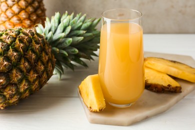 Photo of Tasty pineapple juice in glass and fresh fruits on white wooden table against grey background, closeup