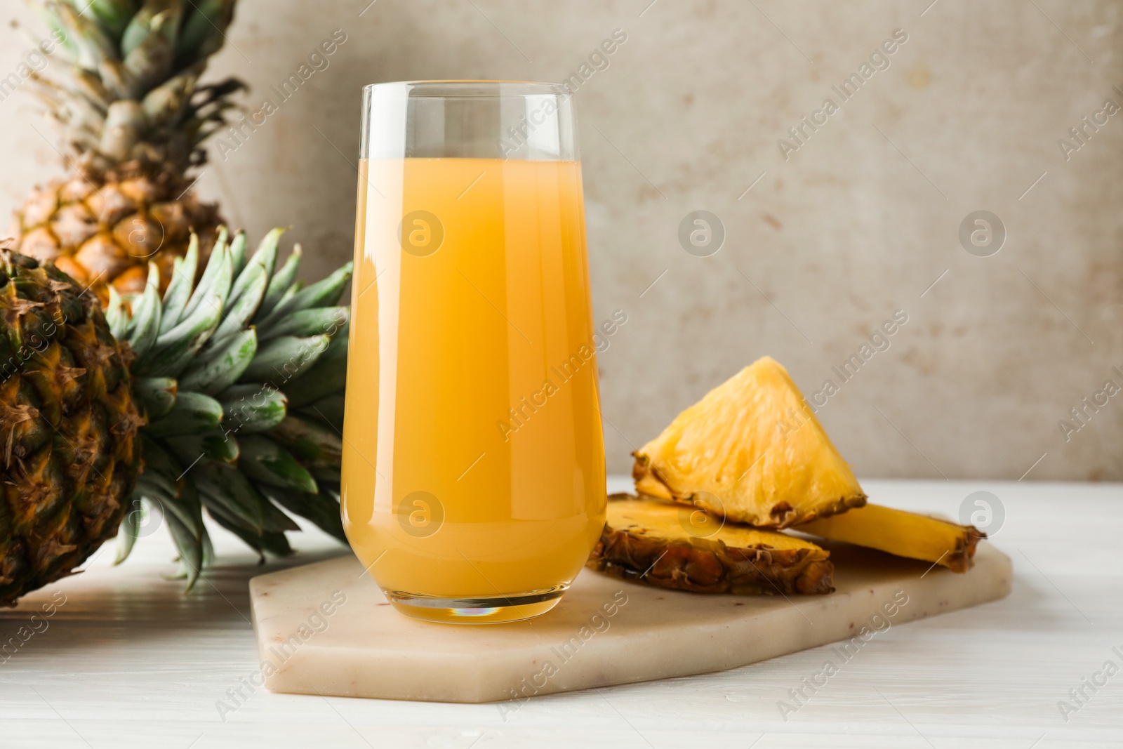 Photo of Tasty pineapple juice in glass and fresh fruits on white wooden table against grey background, closeup